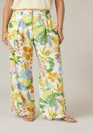 Pantalons larges avec des motifs floraux et de feuilles colorés en jaune, vert, bleu et rose, portés avec des sandales beiges et un haut clair.