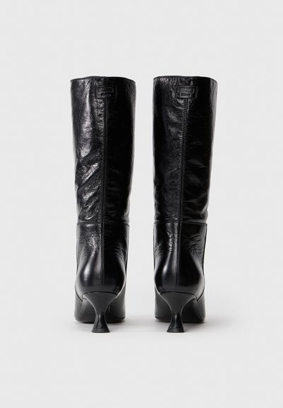 Fekete bőr, középmagas szárú csizmák keskeny sarokkal, hátulról nézve, sima fehér háttéren.