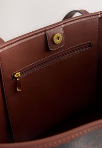 Intérieur d'un sac à main en cuir marron, comprenant une poche zippée avec une ferrure dorée et une fermeture à bouton-pression magnétique. Texture lisse, design minimaliste.