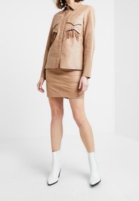 Sammetstonad lädertröja med fransdetaljer, två bröstfickor och silvriga accenter. Matchad med en figursydd läderkjol i samma nyans och vita ankelboots.