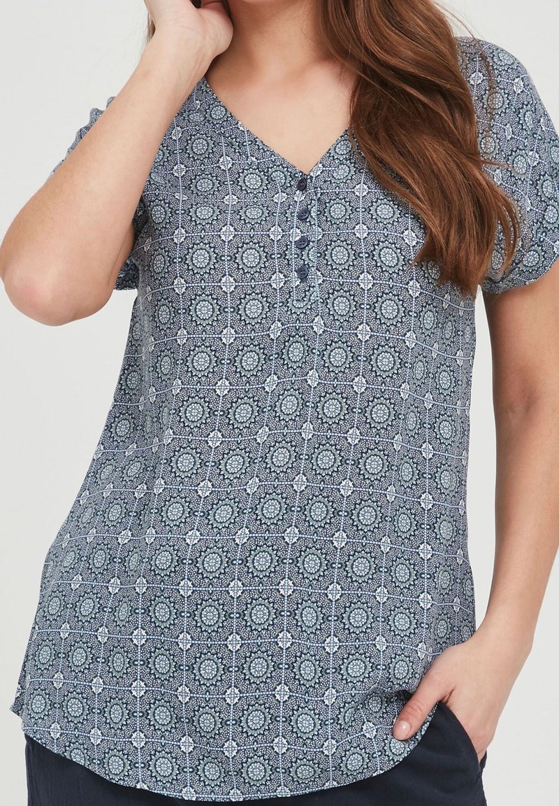 Blouse à manches courtes de couleur bleu marine avec un motif, encolure en V et détail de boutons. Le tissu présente des motifs circulaires et une texture lisse.