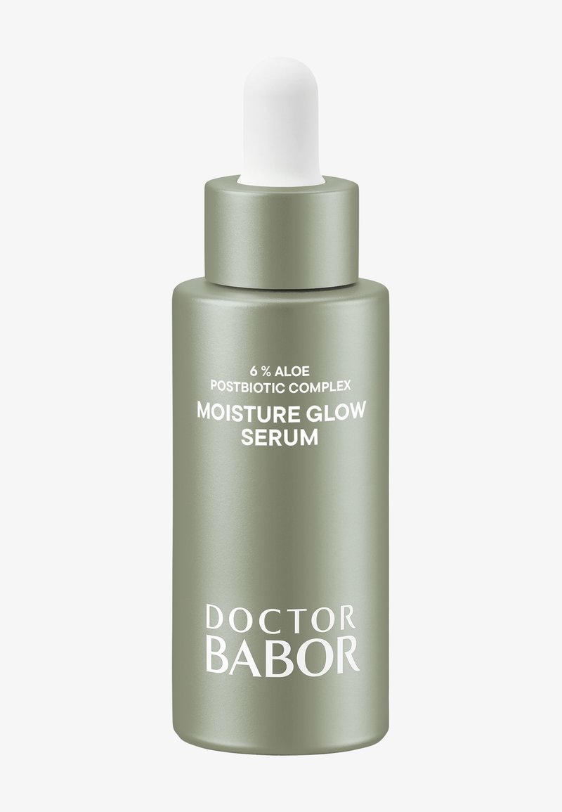 Bottiglia di vetro verde smerigliato con un tappo contagocce bianco. L'etichetta riporta "6% Complesso Postbiotico di Aloe" e "Siero Illuminante Idratante". Il testo è bianco.