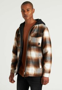 Chaqueta de cuadros marrón y blanca con capucha negra, cierre con cremallera y dos bolsillos delanteros. Presenta una textura cálida y suave, y un diseño casual.