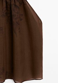 Tissu marron transparent avec un imprimé floral subtil, suspendu lâchement sur un fond blanc.