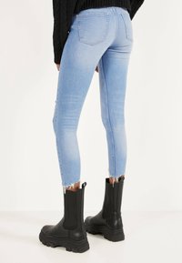 Ljusblå smala jeans med fransade fållar, med bakfickor och en tight passform, kombinerat med svarta kraftiga kängor.