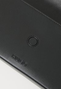 Portefeuille en cuir noir avec logo "Hugo" en relief, détail d'accent rond et texture lisse, mettant en avant un design minimaliste et des coutures précises.
