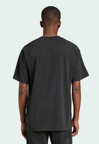 Czarny bawełniany t-shirt o luźnym kroju, z krótkimi rękawami i szwami raglanowymi, o gładkiej fakturze i bez widocznych logo.