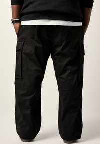 Schwarze Cargo-Hosen mit lockerer Passform, seitlichen Taschen und elastischen Bündchen. Hergestellt aus leichtem, strukturiertem Stoff.