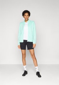 Light mint green zip-up jacket over a white shirt, black shorts, white socks, and black shoes. Features Adidas branding on clothing.