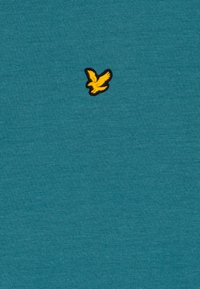 Tamsios žalios medvilnės marškinėliai su mažai išsiuvinėtu geltonu paukščio logotipu kairėje krūtinės pusėje, su lygiu paviršiumi ir klasikinio apvalaus kaklo iškirpte.