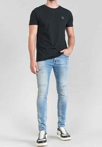 Mustat puuvillapaitat, joissa on pyöreä kaula-aukko, yhdistettynä vaaleansinisiin kuluneisiin slim-fit-farkkuihin ja mustavalkoisiin tennareihin.