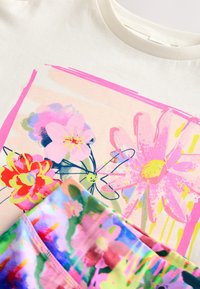 T-shirt à manches courtes couleur crème avec un imprimé floral coloré en rose, rouge et vert, associé à un short à motifs multicolores.