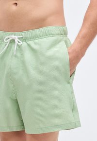 Πράσινα και άσπρα ριγέ μαγιό με ελαστική μέση, κορδόνι και πλαϊνές τσέπες. Λείο ύφασμα.