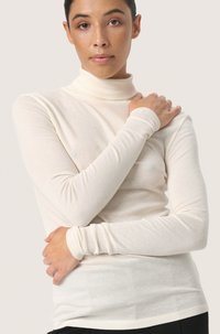 Long-sleeve cream turtleneck made of soft fabric; fitted design with smooth texture and seamless detailing on sleeves and hem.