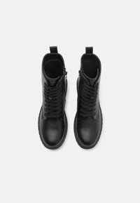 Botas de tobillo de piel negra con punta redondeada, sistema de cordones, cremallera lateral y suela de goma texturizada. Acabado suave con acentos mínimos.