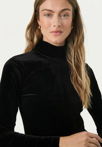 Schwarzes Samt-Turtleneck-Oberteil mit langen Ärmeln, das eine glatte Textur und eine figurbetonte Passform aufweist und eine elegante Silhouette präsentiert.