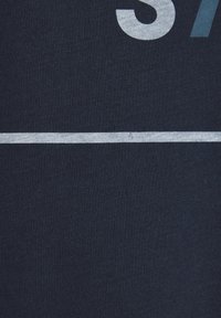 Marineblaue T-Shirt mit einer großen grauen Zahl "37" und einem horizontalen weißen Streifen in der Mitte. Weicher, Baumwollstoff.