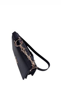 Borsa nera con una texture liscia, dotata di un manico a catena in tonalità oro e lettere decorative lungo il lato. Design compatto e strutturato.