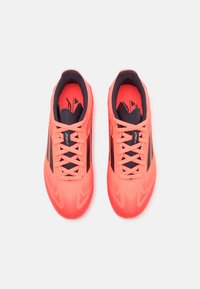 Un par de zapatillas deportivas de color coral brillante con acentos y cordones negros, vistas desde arriba sobre un fondo blanco.