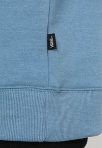 Světlomodrá mikina s žebrovaným lemem a manžetami, vyznačující se texturovanou tkaninou. Na dolním švu má černou štítek s logem Vans.