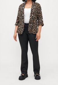 Veste à imprimé léopard avec col à revers, manches trois-quarts et fermeture à un bouton, associée à un pantalon noir élégant et des chaussures noires épaisses.