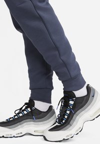 Svarta och grå atletiska sneakers har lager av olika material och accentfärger, med en vit mellansula och synlig luftkudding. Matchade med marinblå byxor.