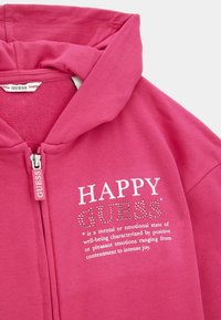 Sudadera con capucha fucsia con cremallera frontal y texto "HAPPY". Adornada con rhinestones y confeccionada en suave tela de algodón.