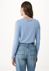 Maglione azzurro chiaro a maniche lunghe con collo rotondo; presenta bottoni decorativi sulle maniche. Abbinato a jeans azzurri chiari a vita alta.