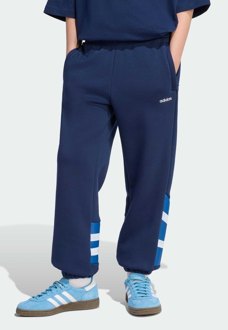 Tmavomodré teplákové nohavice s modro-bielymi pruhovanými akcentmi na manžetách. Majú elastický pás a bočné vrecká. Zobrazené je logo Adidas.