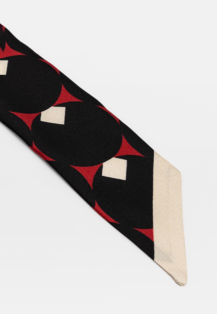 Cravatta stretta in tessuto nero con un motivo geometrico di triangoli rossi e quadrati bianchi, e una punta color crema.