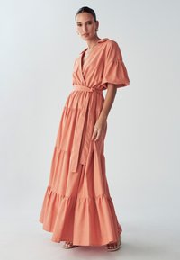 Maxi dress in soft coral cotton, featuring a wrap design, short puff sleeves, tiered skirt, and a tied waist belt.