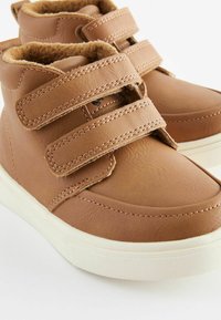 Brązowe skórzane buty typu high-top z dwoma rzepami, wyściółką z miękkiego materiału i białą gumową podeszwą; gładkie i teksturowane powierzchnie.