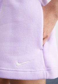 Ljuslila Nike-shorts i mjukt material, med en sidoficka och en vit broderad logotyp vid fållen. Texturerad yta.