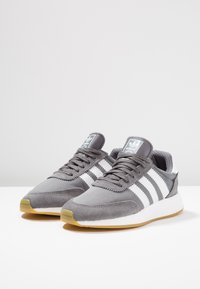 Grå sneakers i mocka och mesh med ett vitt randigt mönster, rund tå och sula i gummirubber. Lätta med en vadderad krage.