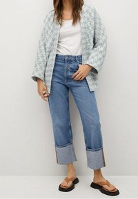 Jasnoniebieska kurtka z wzorem na białym topie, zestawiona z wysokim stanem dżinsów z surowymi wykończeniami na nogawkach oraz brązowymi sandałami. Casualowy look.