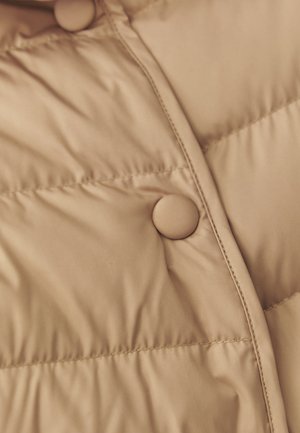 Beige tooniga tikitud kangas kahe ümmarguse nööbi, õmmeldud õmbluste ja polsterdatud tekstuuriga, tõenäoliselt jope või mantli osa.