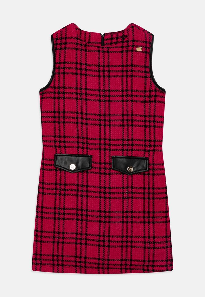 Robe rouge sans manches avec motif écossais noir, emmanchures bordées de noir, deux poches avant en simili cuir noir avec des boutons.