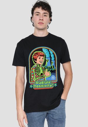 Young man wearing a black T-shirt with a colorful cartoon of a boy showing a thumbs up near nuclear plant cooling towers, captioned "Radiate Positivity!"