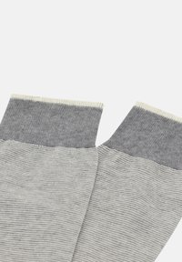 Pelēki adīti zābaciņi ar ribota tipa augšdaļu tumšākā pelēkā tonī. Raksturo gluda tekstūra un kontrastējoša balta svītra augšējā malā.