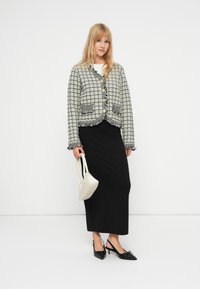 Černobílý vzorovaný blazer s krátkým střihem, třásňovým lemem, zapínáním na knoflík, doplněný černou sukní a krémovou kabelkou.