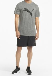 Grå atletisk t-shirt med en svart hoppande kattlogo, ihop med svarta shorts och svarta athletic skor, allt designat för aktiv fritid.