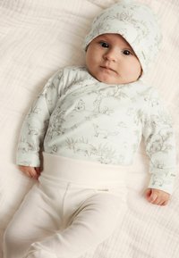 Hellblaues Langarmhemd mit Tierillustrationen, kombiniert mit weißen elastischen Hosen. Ein passendes Cap weist dasselbe Design auf.