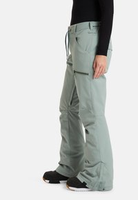 Lichtgroene skibroek van flexibele stof, met ritszakken, een relaxte pasvorm en versterkte zoom, gecombineerd met zwarte schoeisel.