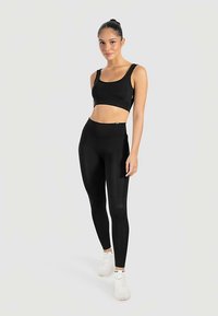 Zwarte sportieve crop top en hooggetailleerde legging met een gladde textuur en een aansluitend ontwerp, gecombineerd met witte sneakers.