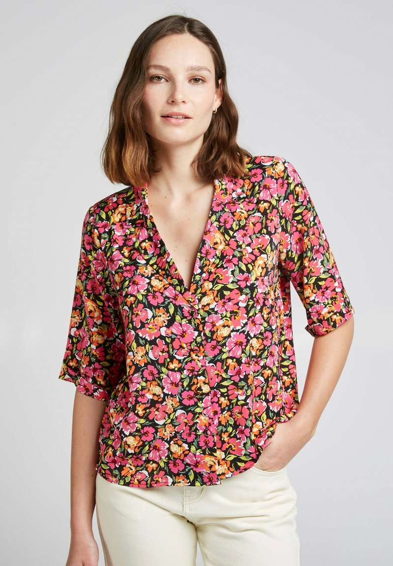 Blouse florale avec un fond noir et des fleurs roses, oranges et jaunes. Elle a un décolleté en V, des manches courtes et une coupe décontractée.