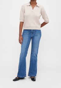 Polo beige à manches courtes avec une finition texturée, associé à un jean évasé bleu clair doté de poches arrière et de détails de couture subtils.