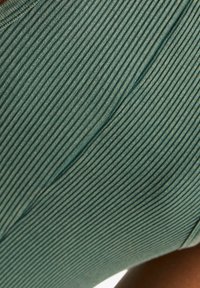 Top in maglia costina di colore verde tenue, con vista ravvicinata che mette in risalto la superficie testurizzata e il design della scollatura senza cuciture.