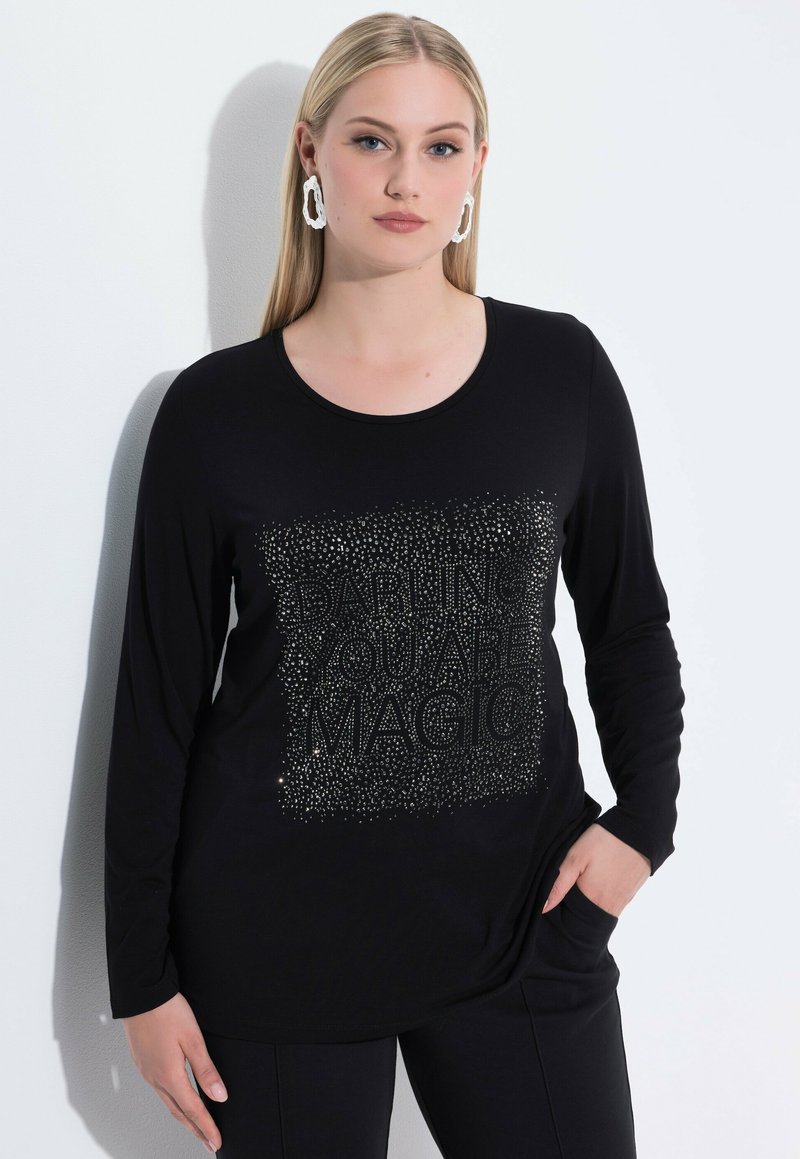 Schwarzes Langarm-T-Shirt mit einem glitzernden Design und dem Text "WAGEMUTIG BIST DU MAGIE", mit rundem Ausschnitt und weichem Stoff.