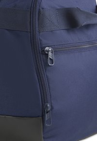 Donkerblauwe stoffen tas met een ritssluiting, gestructureerd materiaal, versterkte stiksels en een zwarte onderzijde voor duurzaamheid.