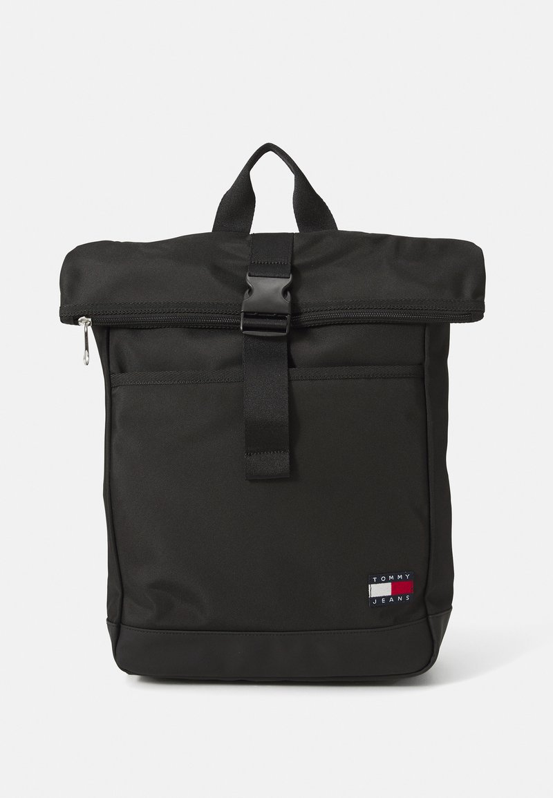 Rucsac negru din material textil, cu un design cu garnitură glisantă, închidere cu fermoar și un buzunar frontal. Include o curea rezistentă și un mic etichetă cu logo.